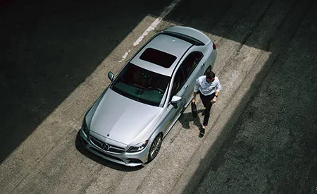 An overhead shot of a man walking beside a parked silver Mercedes-Benz.