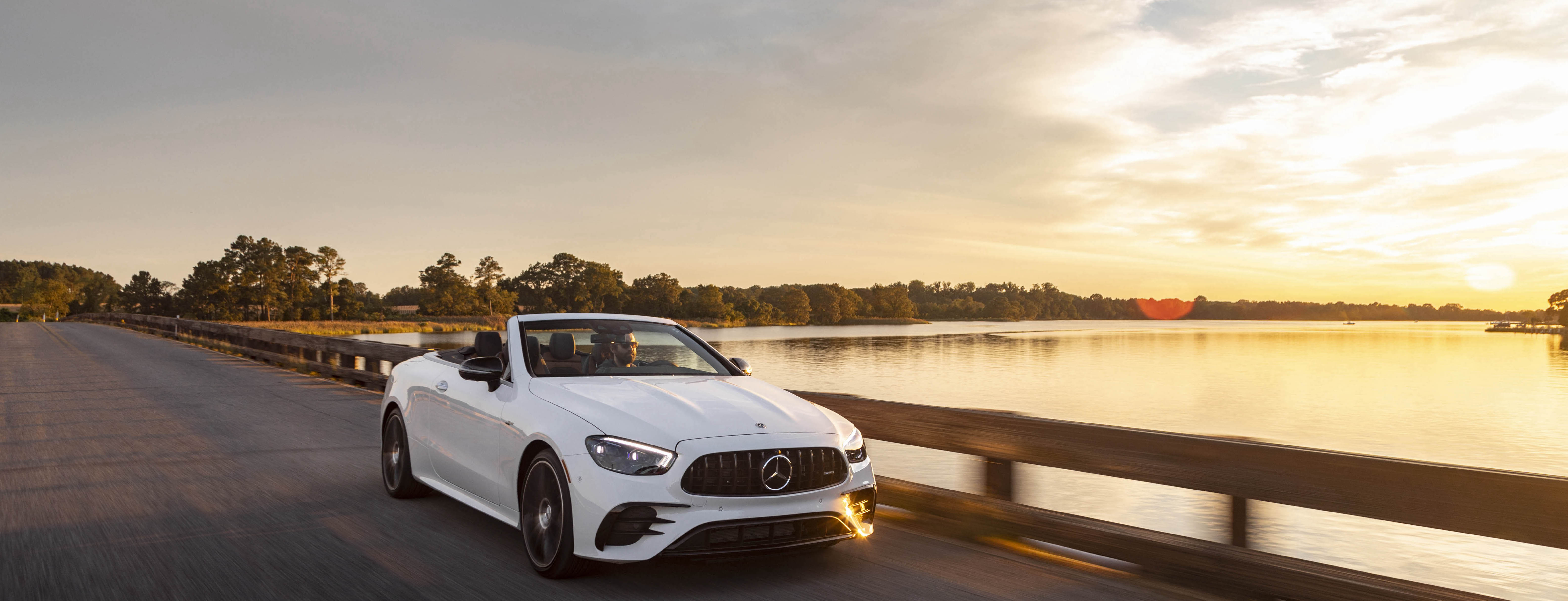 A white E Cabriolet driving down a road at sunset