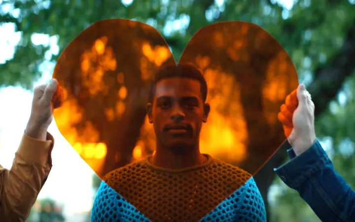 Young mans face behind transparent heart held by two other hands