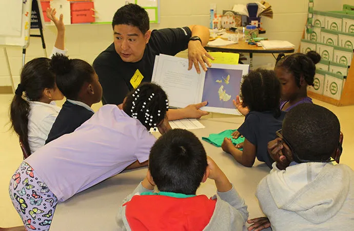 A volunteer is visiting a local school, reading to the children and answering their questions.