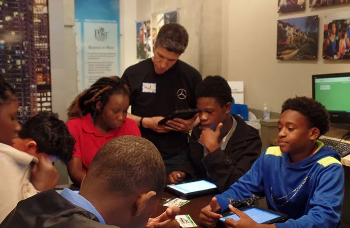 A group of high school students are using iPads while their mentor provides instruction and assistance.