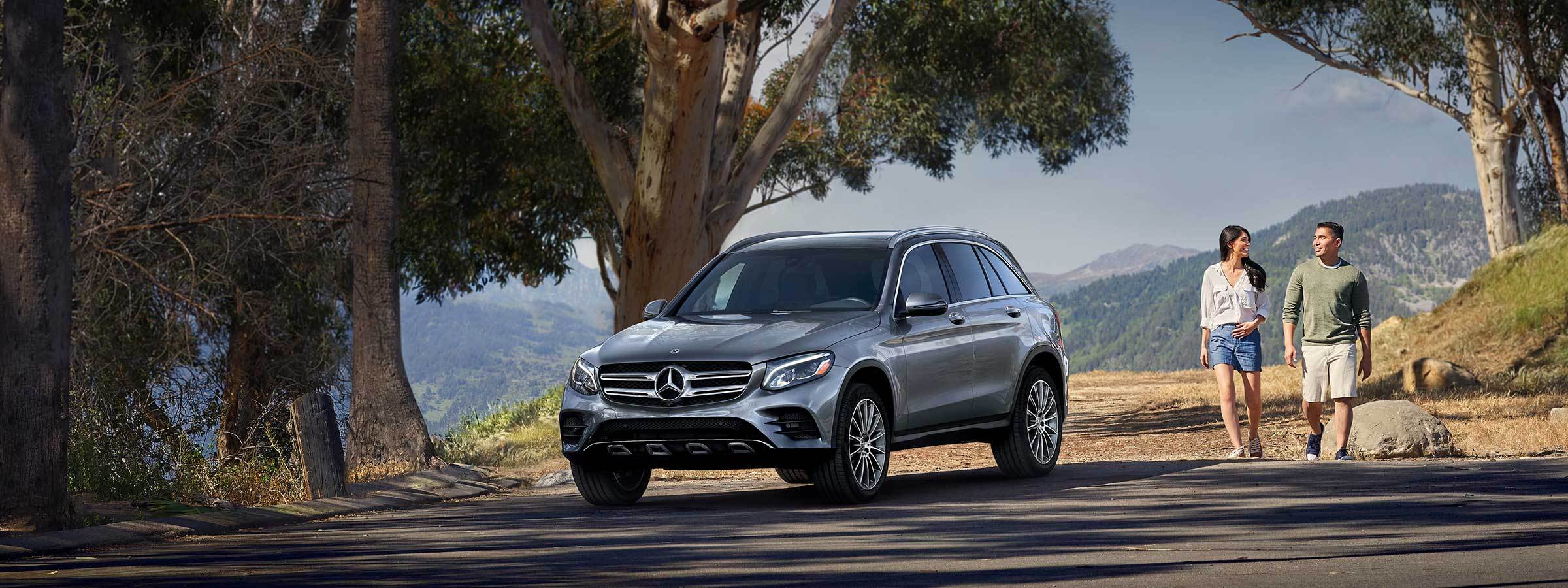 A Silver GLC SUV parked along side a walking trail with a couple approaching