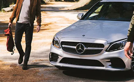 A man with a bag walks beside a parked Mercedes-Benz sedan.