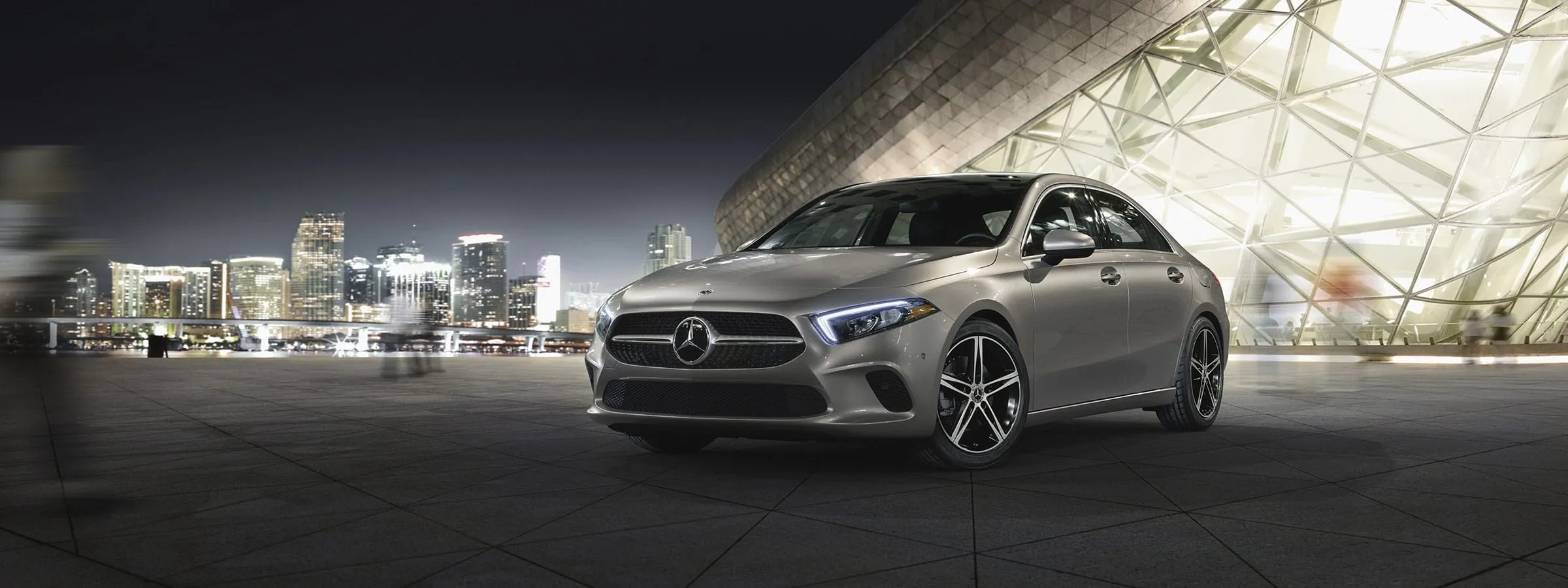 The 2021 A-Class Sedan in Iridium Silver with AMG Line Exterior and LED lights parked in the snow.