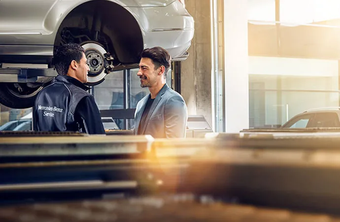 A service technician talks with a Mercedes-Benz owner as he works on his vehicle.