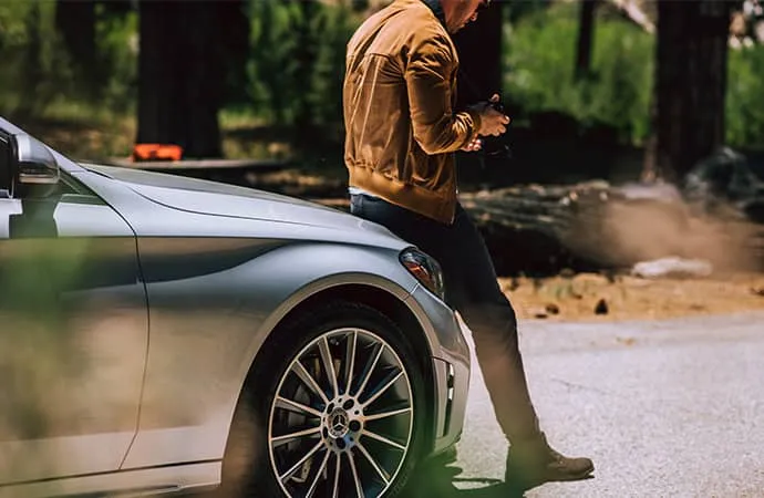 A driver leans on the hood of his Mercedes-Benz as he checks his phone.