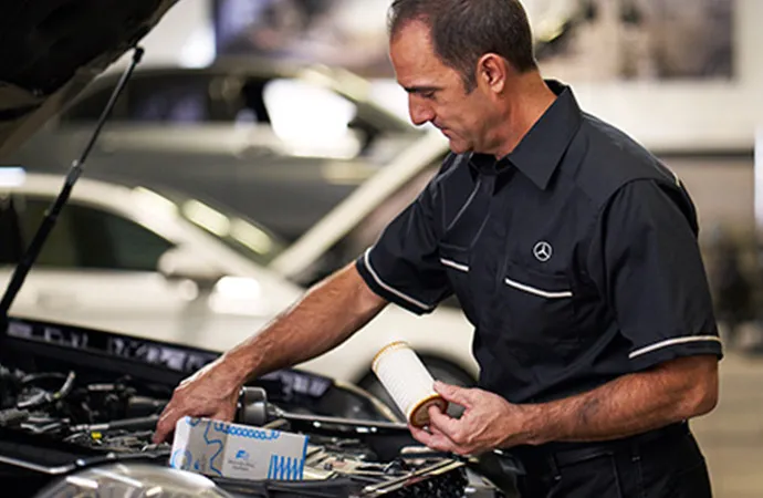A mechanic installs an air filter under the hood of a car.