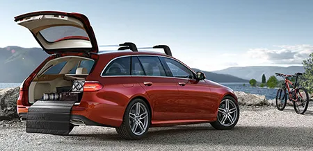 A red E-Class Wagon is parked lakeside with the trunk open.