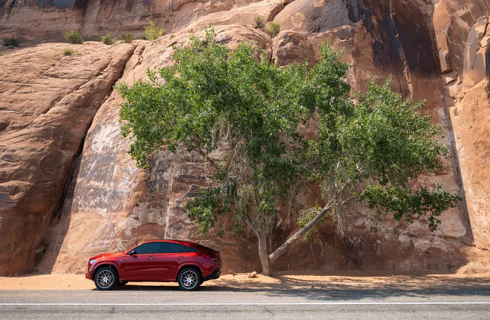 A red Mercedes-Benz is parked under a tree.