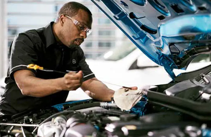 A Mercedes-Benz service technician is checking the oil.
