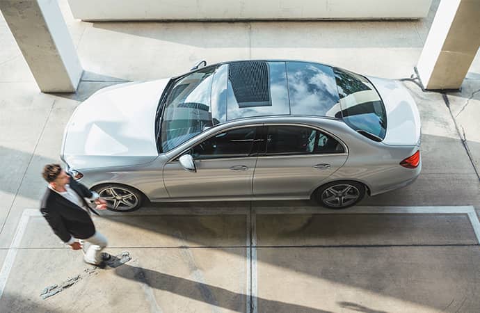 An overhead shot of a man strolling past a silver Mercedes-Benz.
