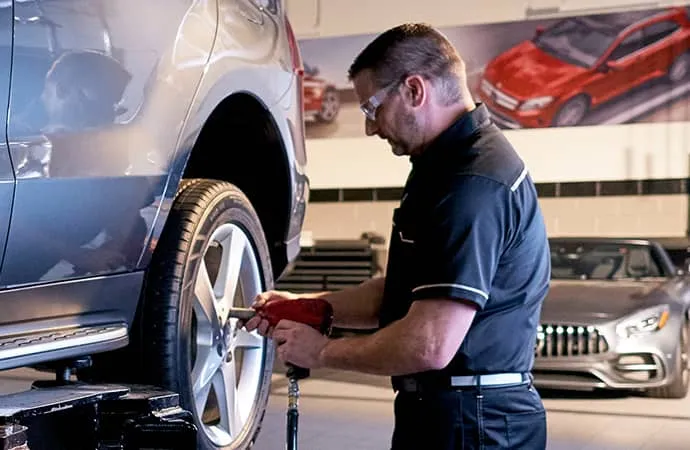 A Mercedes-Benz service technician works on the rear wheel of a vehicle.