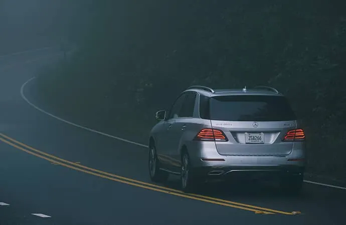 A GLE SUV is shown from behind as it navigates a foggy road at night.