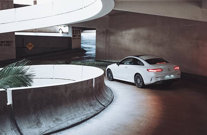 A white Mercedes-Benz coupe descends the ramp of a parking garage.