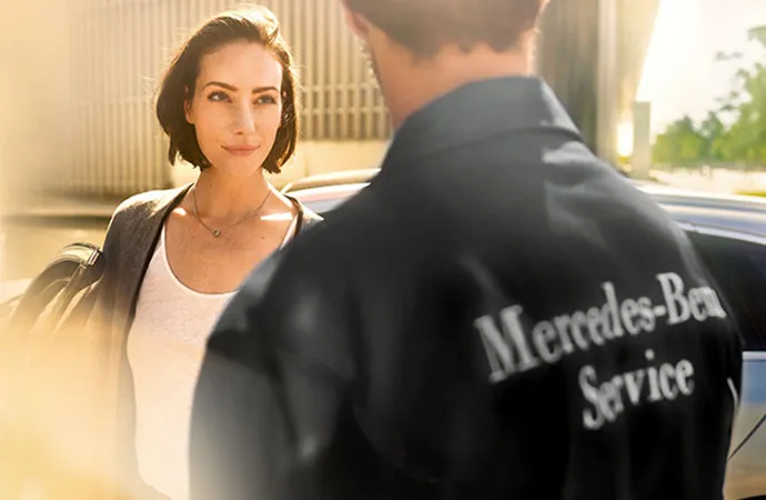 A woman is being approached by a Mercedes-Benz service technician.