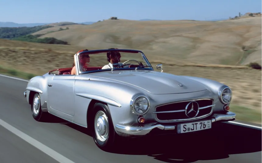 A silver 190 SL is driven along a country road with the top down.